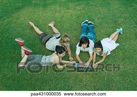 Group of young friends lying on grass, using laptop View Large Photo Image Stock Photography - Group of young friends lying on grass, using laptop. Fotosearch