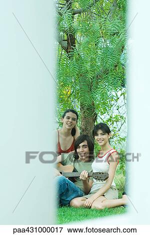 Group of young friends sitting by tree together, one playing guitar View Large Photo Image Stock Photo - Group of young friends sitting by tree together, one playing guitar. Fotosearch