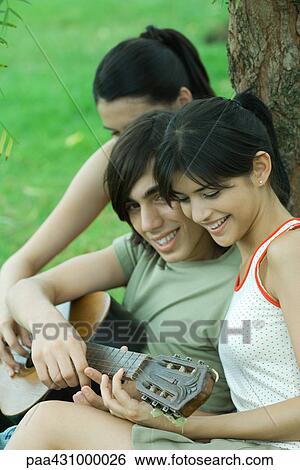 Group of young friends sitting by tree with guitar View Large Photo Image Stock Photograph - Group of young friends sitting by tree with guitar. Fotosearch