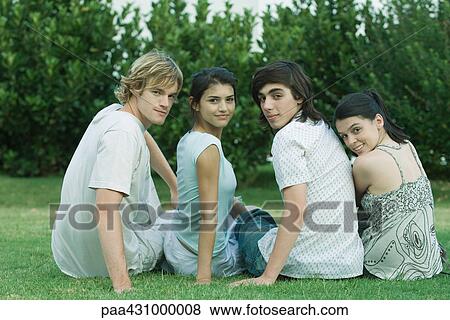 Group of young friends sitting on grass, looking over shoulders at camera View Large Photo Image Stock Photo - Group of young friends sitting on grass, looking over shoulders at camera. Fotosearch