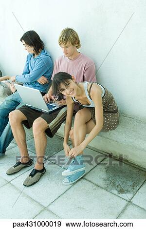 Group of young friends sitting on bench, one young woman tying shoe laces and smiling at camera View Large Photo Image Stock Photo - Group of young friends sitting on bench, one young woman tying shoe laces and smiling at camera. Fotosearch
