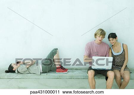 Stock Image - Group of young friends using laptop and cell phone. Fotosearch