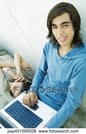 Stock Photo - Teen boy using laptop while female friend uses cell phone. Fotosearch