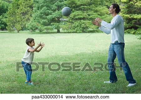 Picture - Boy and father outdoors, throwing ball back and forth on a grassy lawn. Fotosearch