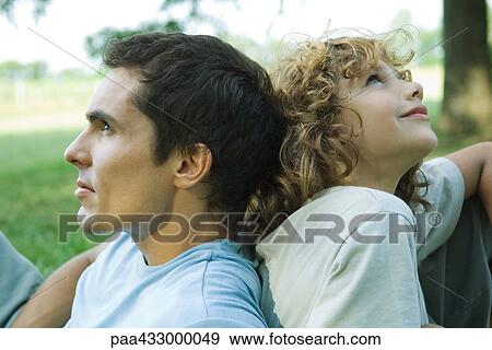 Stock Photo - Boy and father sitting back to back, close-up. Fotosearch