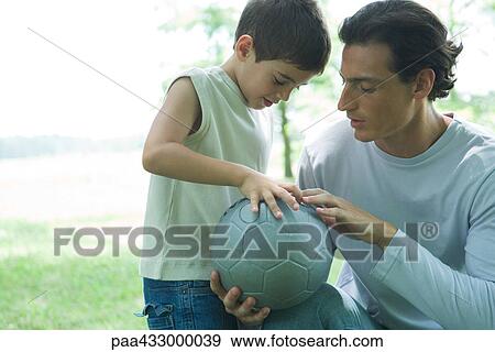 Stock Photo - Boy looking at soccer ball with father. Fotosearch