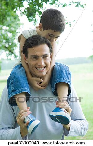 Stock Image - Boy riding on father's shoulders, both smiling. Fotosearch