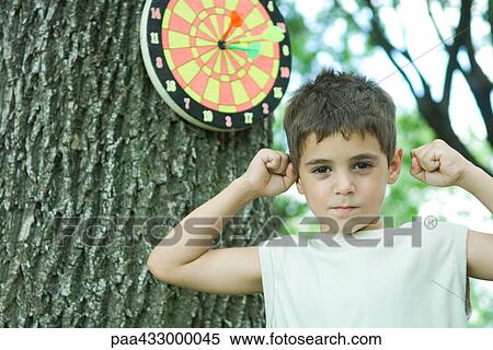 Stock Photography - Boy standing next dart board, raising fists. Fotosearch