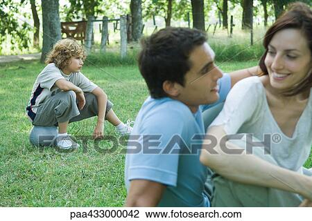 Family sitting on grass outdoors, focus on boy sitting on ball in background View Large Photo Image Stock Image - Family sitting on grass outdoors, focus on boy sitting on ball in background. Fotosearch