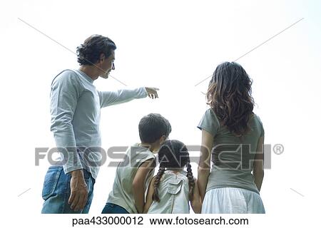 Stock Image - Family standing looking at sky, rear view, low angle view. Fotosearch