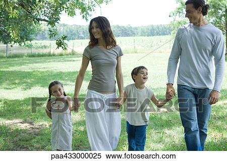 Stock Photography - Family walking across grass, holding hands. Fotosearch
