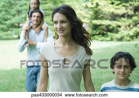 Picture - Family walking across lawn, focus on mother in foreground. Fotosearch