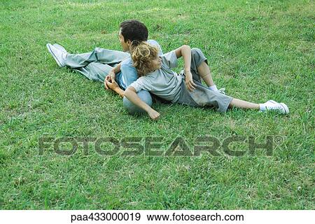 Stock Photo - Father and boy sitting back to back on grass. Fotosearch