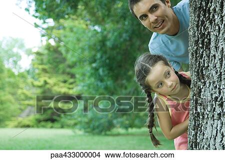 Father and daughter peeking around tree trunk View Large Photo Image Picture - Father and daughter peeking around tree trunk. Fotosearch
