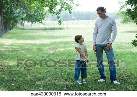 Stock Photography - Father and son standing outside on grass, looking at each other. Fotosearch