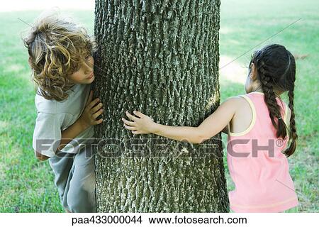 Girl and boy standing on either side of tree trunk, peeking around View Large Photo Image Picture - Girl and boy standing on either side of tree trunk, peeking around. Fotosearch