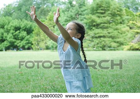 Stock Image - Girl standing on grass with arms in air. Fotosearch