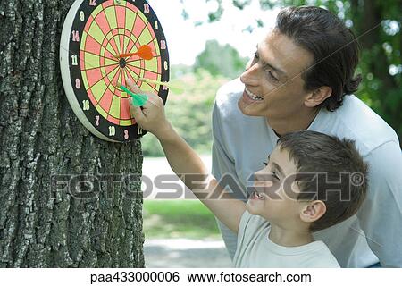 Man and boy looking at dartboard hanging on tree View Large Photo Image Stock Photograph - Man and boy looking at dartboard hanging on tree. Fotosearch