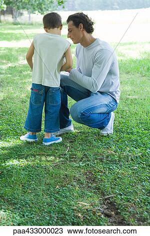 Stock Image - Man crouching next to boy, outdoors. Fotosearch