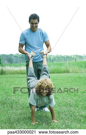 Stock Image - Man holding boy's feet while boy balances on hands. Fotosearch