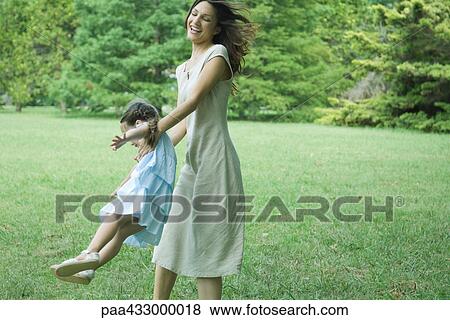 Stock Photo - Woman swinging daughter around on grass. Fotosearch