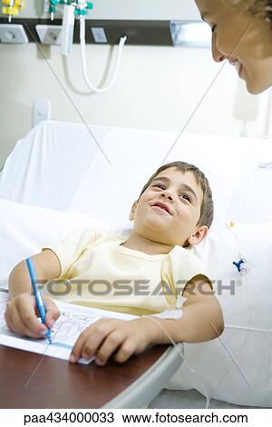 Boy lying in bed coloring, smiling up at woman View Large Photo Image Stock Image - Boy lying in bed coloring, smiling up at woman. Fotosearch