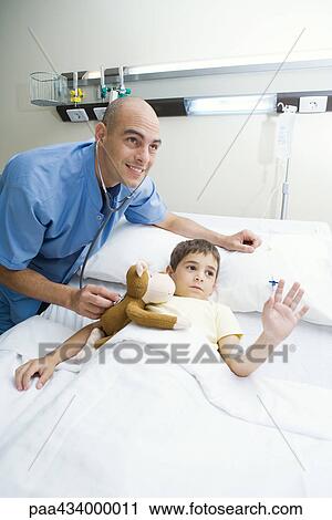 Boy lying in hospital bed, intern holding stethoscope to boy's stuffed animal, both looking out of frame View Large Photo Image Stock Image - Boy lying in hospital bed, intern holding stethoscope to boy's stuffed animal, both looking out of frame. Fotosearch
