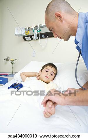 Stock Image - Boy lying in hospital bed, intern holding boy's arm. Fotosearch