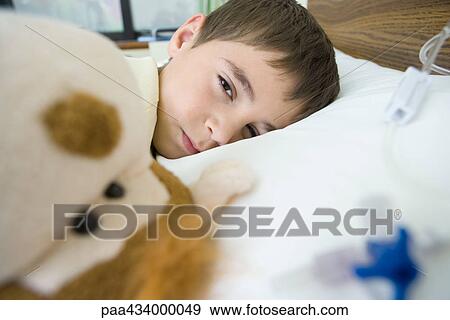 Boy lying in hospital bed, looking at camera through half closed eyes View Large Photo Image Stock Photo - Boy lying in hospital bed, looking at camera through half closed eyes. Fotosearch