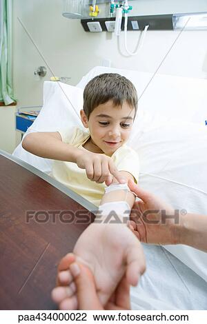 Boy lying in hospital bed touching IV tube while man holds boy's arm View Large Photo Image Stock Image - Boy lying in hospital bed touching IV tube while man holds boy's arm. Fotosearch