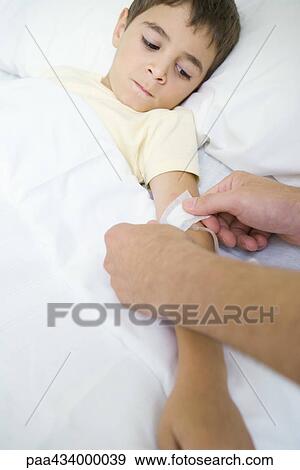 Boy lying in hospital bed watching man put bandage over IV tube View Large Photo Image Stock Photo - Boy lying in hospital bed watching man put bandage over IV tube. Fotosearch