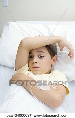Boy lying in hospital bed with arm across forehead, looking away View Large Photo Image Stock Photo - Boy lying in hospital bed with arm across forehead, looking away. Fotosearch