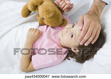 Girl lying in bed with teddy bear, man holding her hand on putting other hand on her forehead View Large Photo Image Stock Photo - Girl lying in bed with teddy bear, man holding her hand on putting other hand on her forehead. Fotosearch