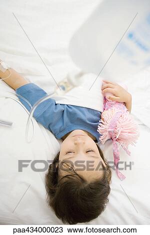 Girl lying in hospital bed holding doll View Large Photo Image Stock Image - Girl lying in hospital bed holding doll. Fotosearch