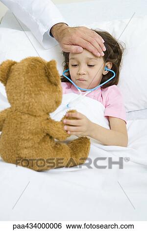 Girl lying in hospital bed, holding teddy bear, doctor's hand on forehead View Large Photo Image Stock Photograph - Girl lying in hospital bed, holding teddy bear, doctor's hand on forehead. Fotosearch
