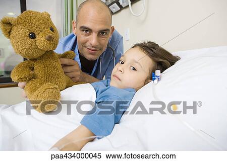 Girl lying in hospital bed, male intern next to her holding up teddy bear View Large Photo Image Stock Photography - Girl lying in hospital bed, male intern next to her holding up teddy bear. Fotosearch