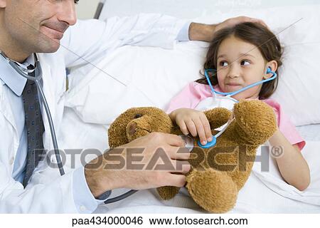 Girl lying in hospital bed, smiling at doctor as both hold stethoscopes to girl's stuffed animal View Large Photo Image Stock Photograph - Girl lying in hospital bed, smiling at doctor as both hold stethoscopes to girl's stuffed animal. Fotosearch