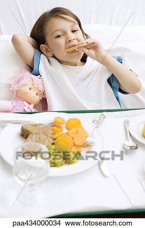 Girl lying in hospital bed with food tray in front of her, eating cookie View Large Photo Image Picture - Girl lying in hospital bed with food tray in front of her, eating cookie. Fotosearch