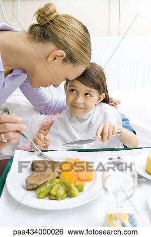 Girl sitting in hospital bed smiling up at mother while eating meal View Large Photo Image Stock Photograph - Girl sitting in hospital bed smiling up at mother while eating meal. Fotosearch
