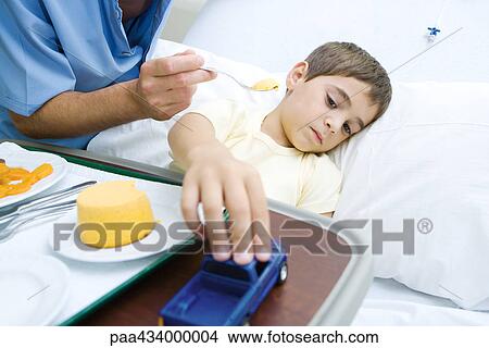 Intern feeding boy in hospital bed View Large Photo Image Picture - Intern feeding boy in hospital bed. Fotosearch