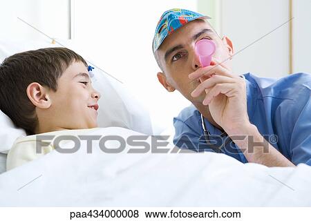 Intern next to boy in hospital bed, wearing mask and blowing party horn View Large Photo Image Stock Photo - Intern next to boy in hospital bed, wearing mask and blowing party horn. Fotosearch