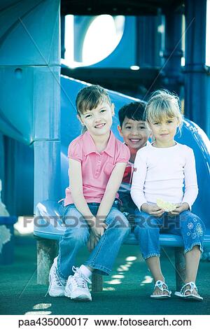 Stock Photo - Children sitting on end of slide, smiling at camera. Fotosearch