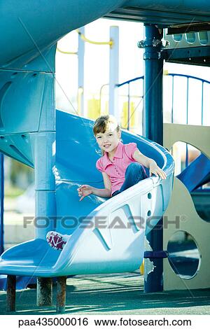 Stock Photograph - Girl going down playground slide, smiling at camera. Fotosearch