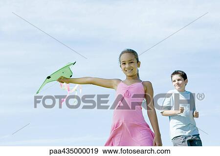 Girl holding out kite, boy in background View Large Photo Image Stock Photo - Girl holding out kite, boy in background. Fotosearch