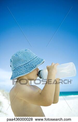 Stock Photo - Boy drinking from water bottle on beach. Fotosearch