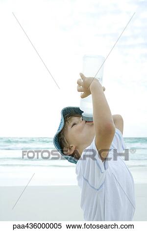 Stock Photography - Boy drinking from water bottle on beach. Fotosearch
