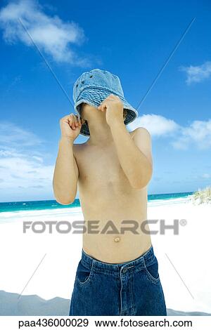 Stock Photo - Boy pulling hat down over face on beach. Fotosearch
