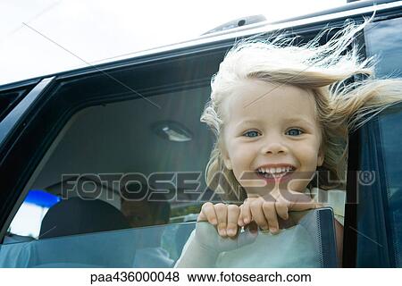Stock Photo - Little girl in car, looking out of window, smiling at camera, hair blowing in wind. Fotosearch