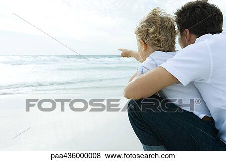 Stock Photo - Man looking at ocean with son, rear view. Fotosearch