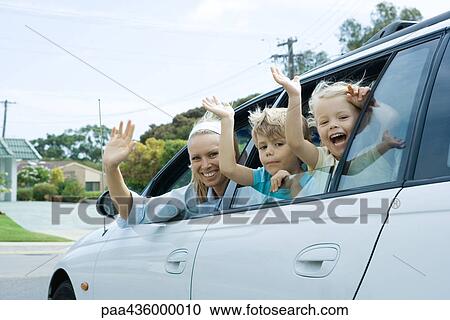 Stock Image - Mother and two children waving out of car windows, looking at camera. Fotosearch